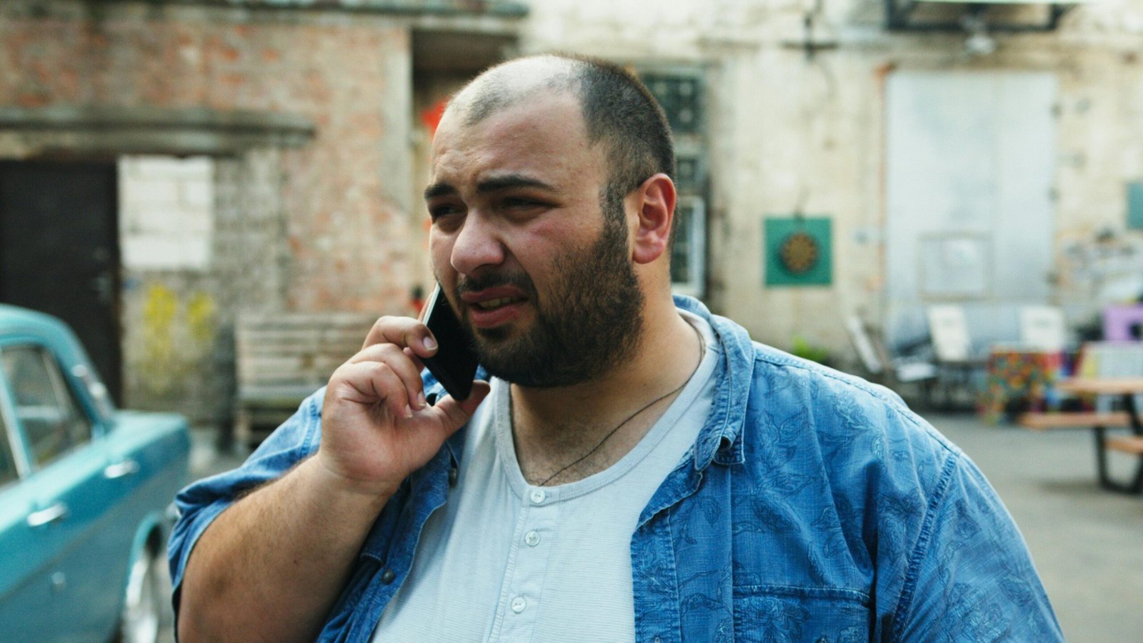 Bearded man with denim shirt using smartphone outside in urban setting.
